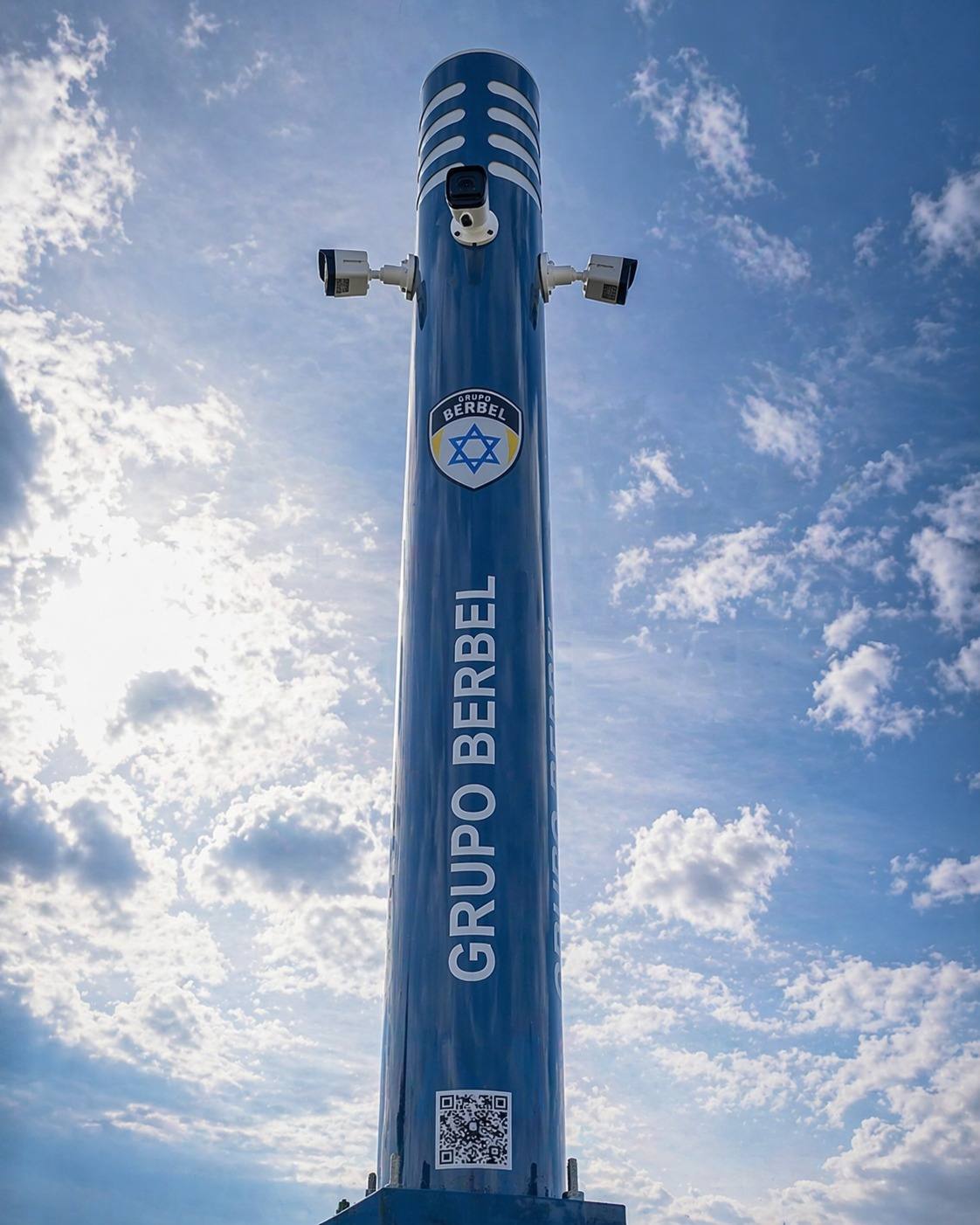 Totem de monitoramento do Grupo Berbel com câmeras e o escudo do grupo, visto de baixo contra o céu